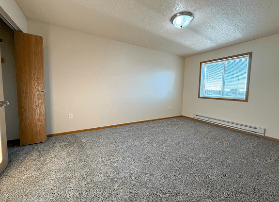A room with a carpeted floor, a window with blinds, and a door.
