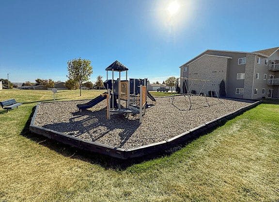 A playground with a swing set and a slide in the foreground and apartment buildings in the background.