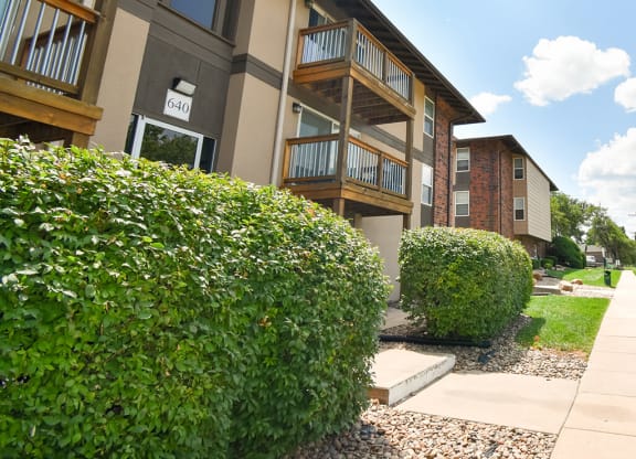 an apartment building with a sidewalk and hedges in front of it