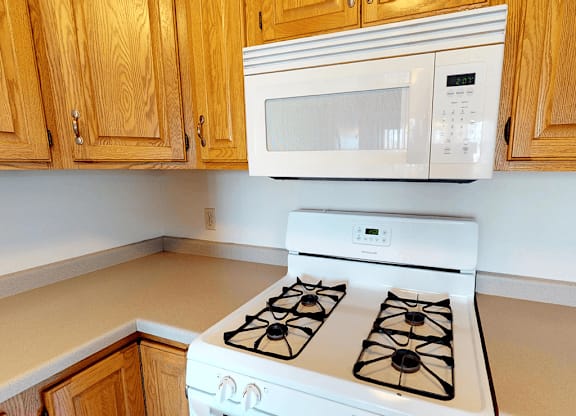 A white microwave oven is mounted above a white gas stove in a kitchen.
