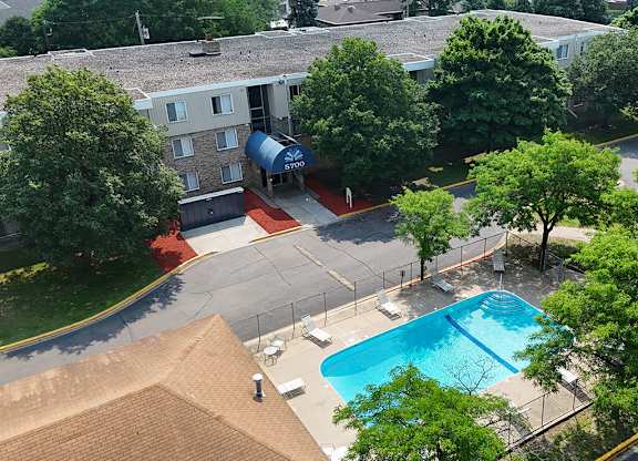 A pool surrounded by trees and a building with a blue awning.