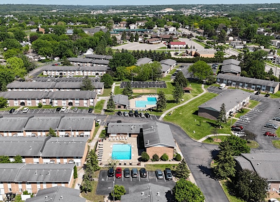 A bird's eye view of a residential area with apartment buildings, a swimming pool, and a parking lot.