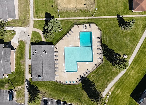 A swimming pool in a grassy area surrounded by a parking lot.