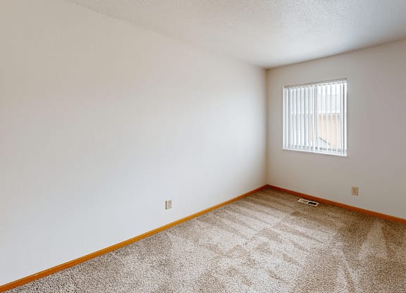 A room with a carpeted floor and a window with blinds.