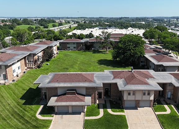 A large house with a brown roof is surrounded by smaller houses and green grass.
