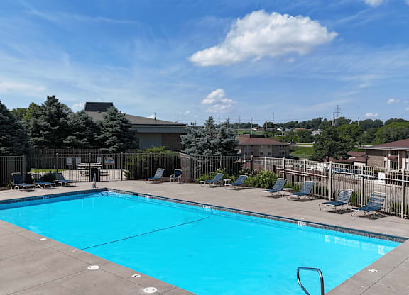 A large blue swimming pool surrounded by a fence and lounge chairs.