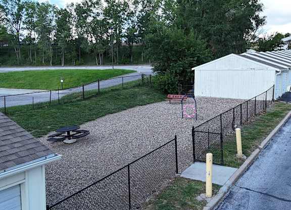 A white shed sits behind a black fence in a grassy area.