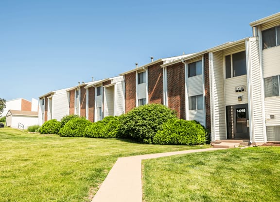 an apartment building with a green lawn and a sidewalk