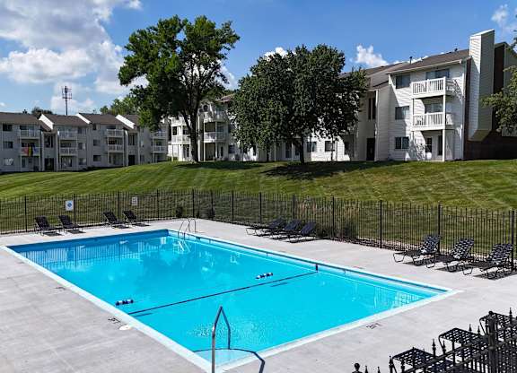 A swimming pool surrounded by chairs and apartment buildings.