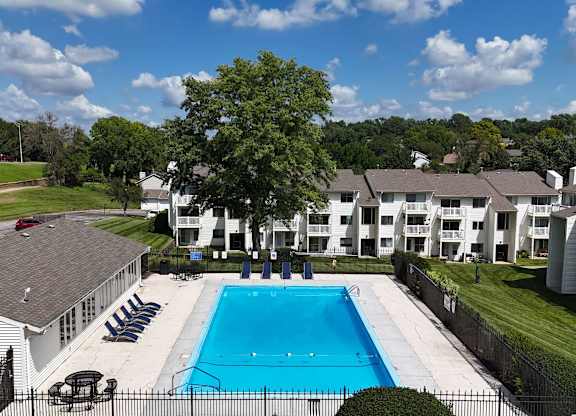 A swimming pool surrounded by a fence and chairs with apartment buildings in the background.