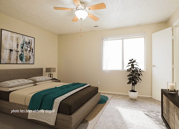 A bedroom with a bed, a ceiling fan, and a plant.