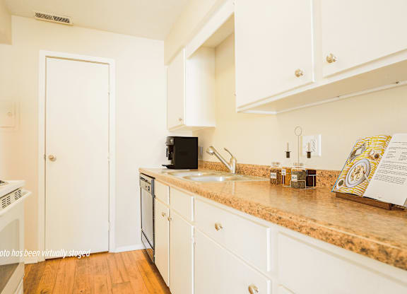 A kitchen with white cabinets and a countertop with a sink and a coffee maker.