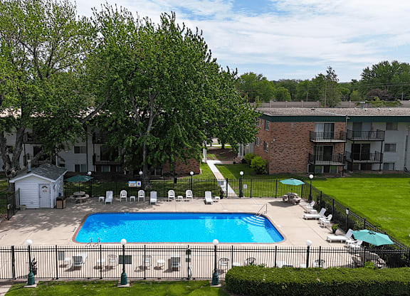 A pool surrounded by lawn chairs and trees.