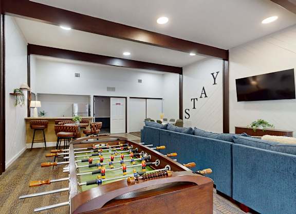A foosball table is in the middle of a room with a couch and a TV.