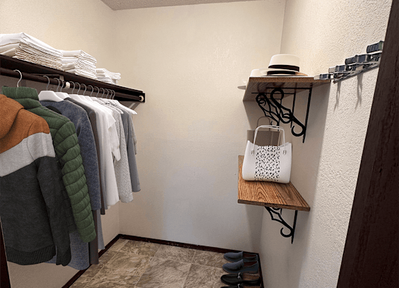 A small closet with clothes hanging and a shelf with a hat and a bag.