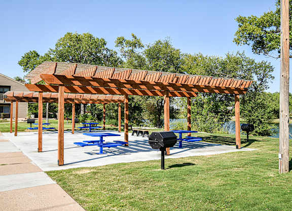 A wooden pergola with blue picnic tables underneath it.