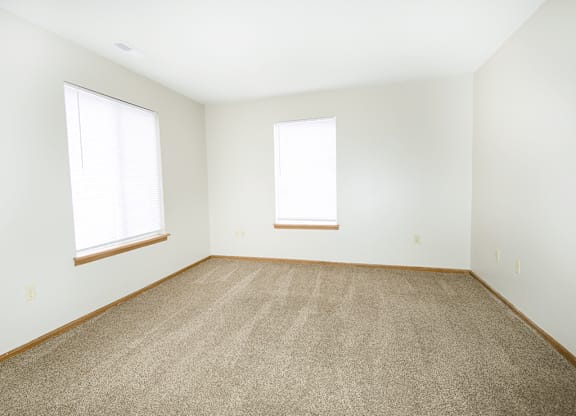 A room with carpeted floor and two windows.