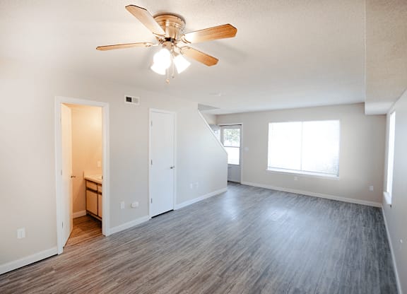 A room with a ceiling fan and light fixture, hardwood floors, and a window with white walls.