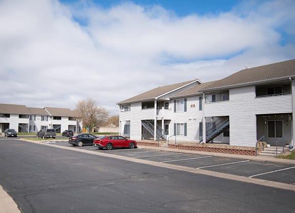 A parking lot with a red car parked in front of a white building.