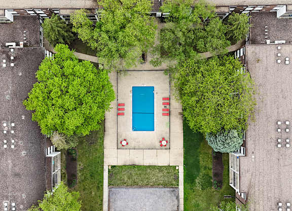 A pool surrounded by trees and grass in a parking lot.