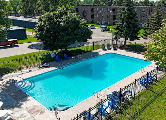 A small pool surrounded by a black fence with blue chairs around it.