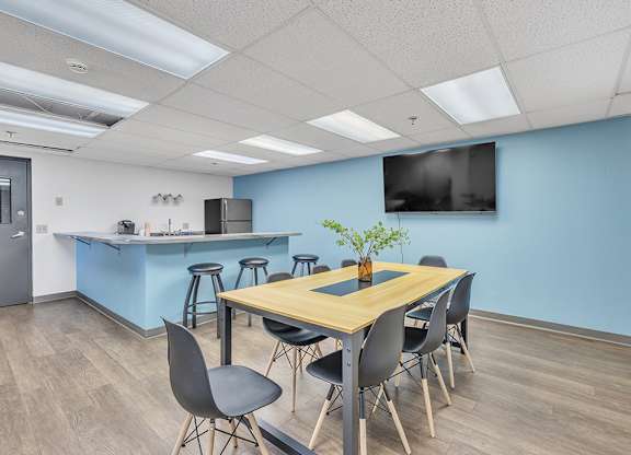 a conference room with a table and chairs with a kitchenette in the background