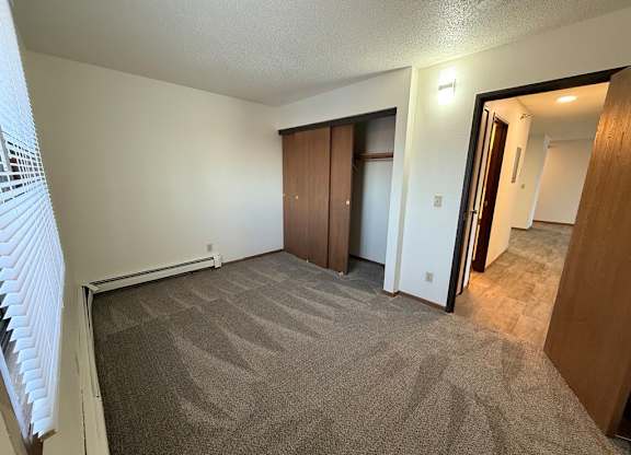 A room with carpeted floor and a window with blinds.