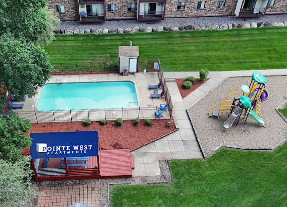A playground area with a slide and swings is located next to a pool at Pointe West Apartments.