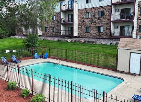 A pool surrounded by a black fence and a building in the background.