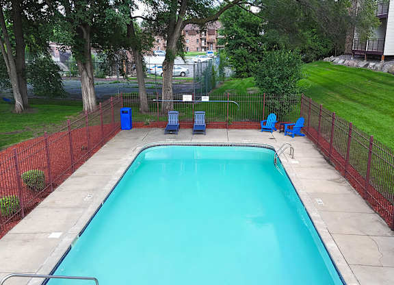 A small pool surrounded by a red fence and blue chairs.