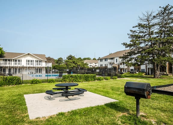 a picnic table and grill sit on a concrete slab in a grassy area with a pool