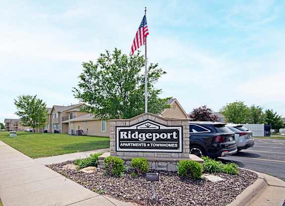 A sign for Ridgeport Apartments and Townhomes with an American flag in the background.