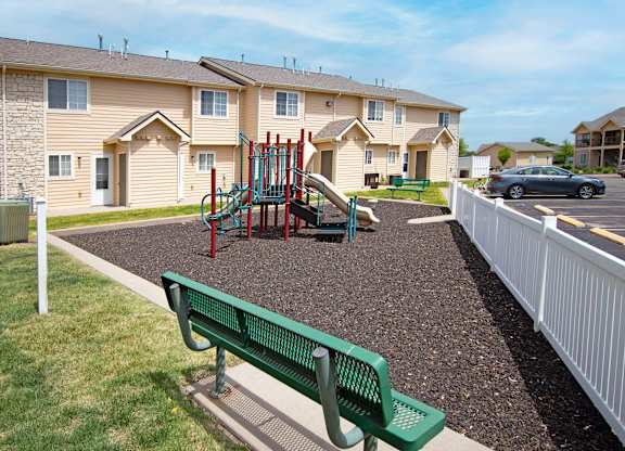 A playground with a green bench and a slide in front of apartment buildings.