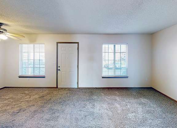A room with a carpeted floor, two windows, and a door.
