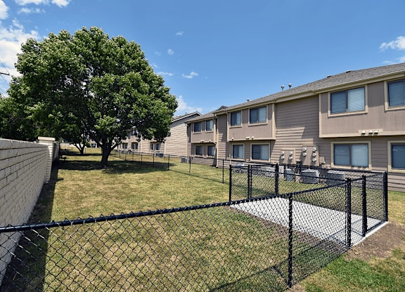 A black fence surrounds a grassy area in front of apartment buildings.