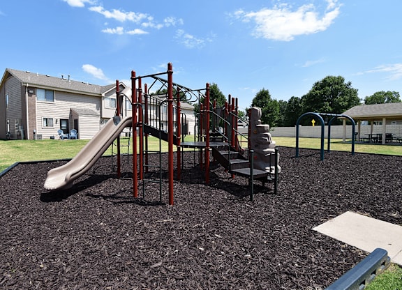 A playground with a red slide and a brown play structure.