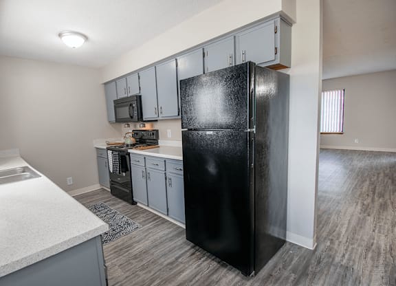 A black refrigerator stands in a kitchen with grey cabinets and a white counter.