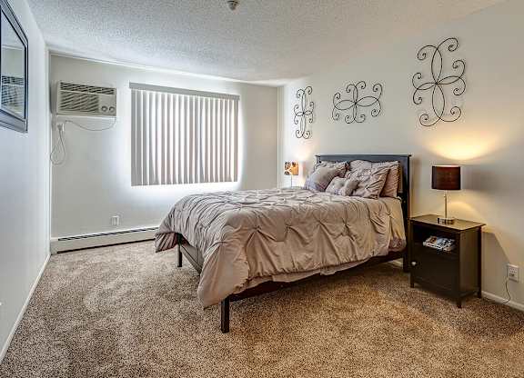 A bedroom with a bed, nightstand, and window with blinds.