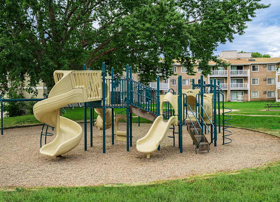 A playground with a yellow slide and a green fence.