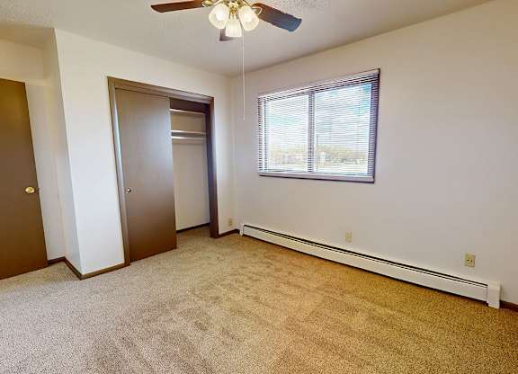 A room with a carpeted floor, a ceiling fan, and a window with blinds.