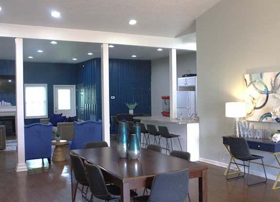 a room with a table and chairs and a kitchen in the background