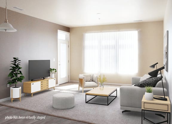 A living room with a grey couch, a white side table, and a wooden cabinet with a flat screen TV on top.