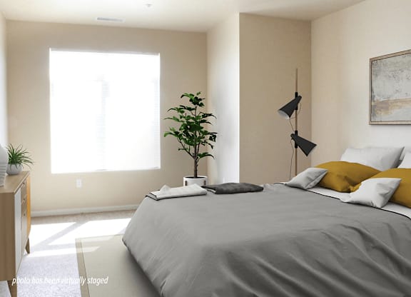 A bedroom with a bed, pillows, a plant, and a lamp.