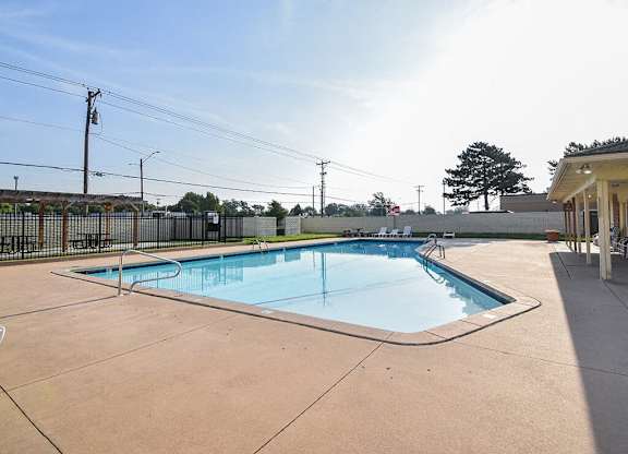 A large outdoor swimming pool with a concrete deck and a fence surrounding it.