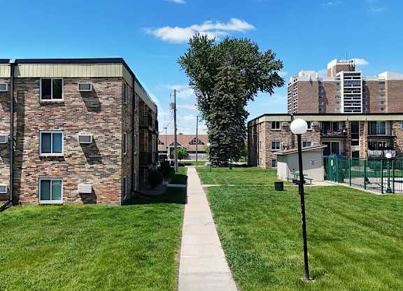 A walkway between two buildings with a green fence and a tree in the background.