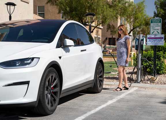 A woman is standing next to a white Tesla car at a charging station. at Habitat @ DTLV, Nevada, 89106