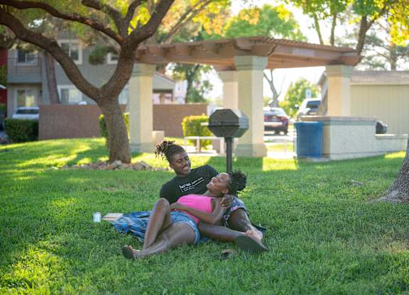 Two people are sitting on the grass under a tree.