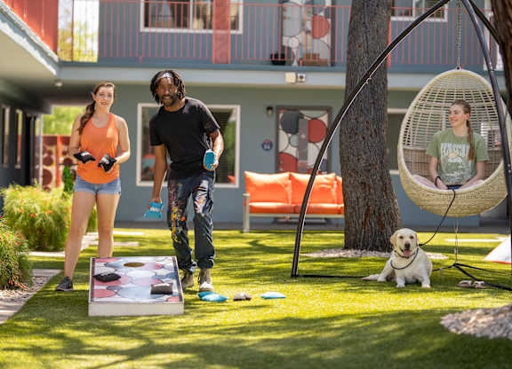 A man and a woman are playing a game on the lawn with a dog sitting under a hanging chair.
