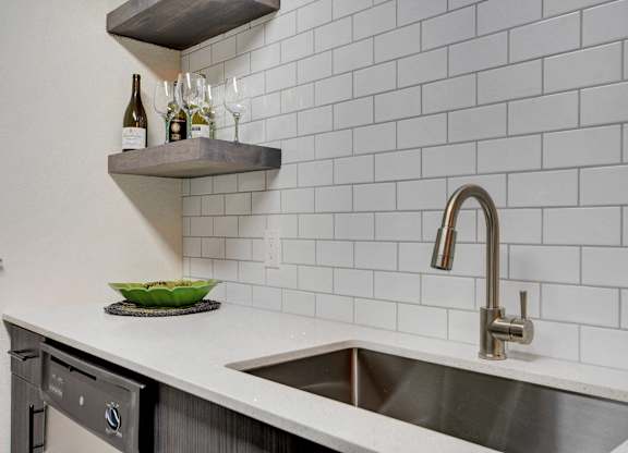 A kitchen with a white tiled wall and a stainless steel sink.