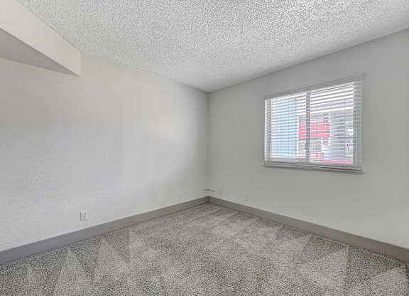 A room with a carpeted floor and a window with blinds.